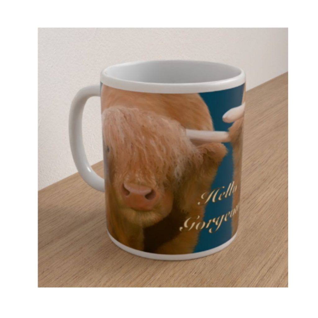 Angled white ceramic mug featuring a shaggy Highland cow with long horns and the words Hello Gorgeous on a teal background.